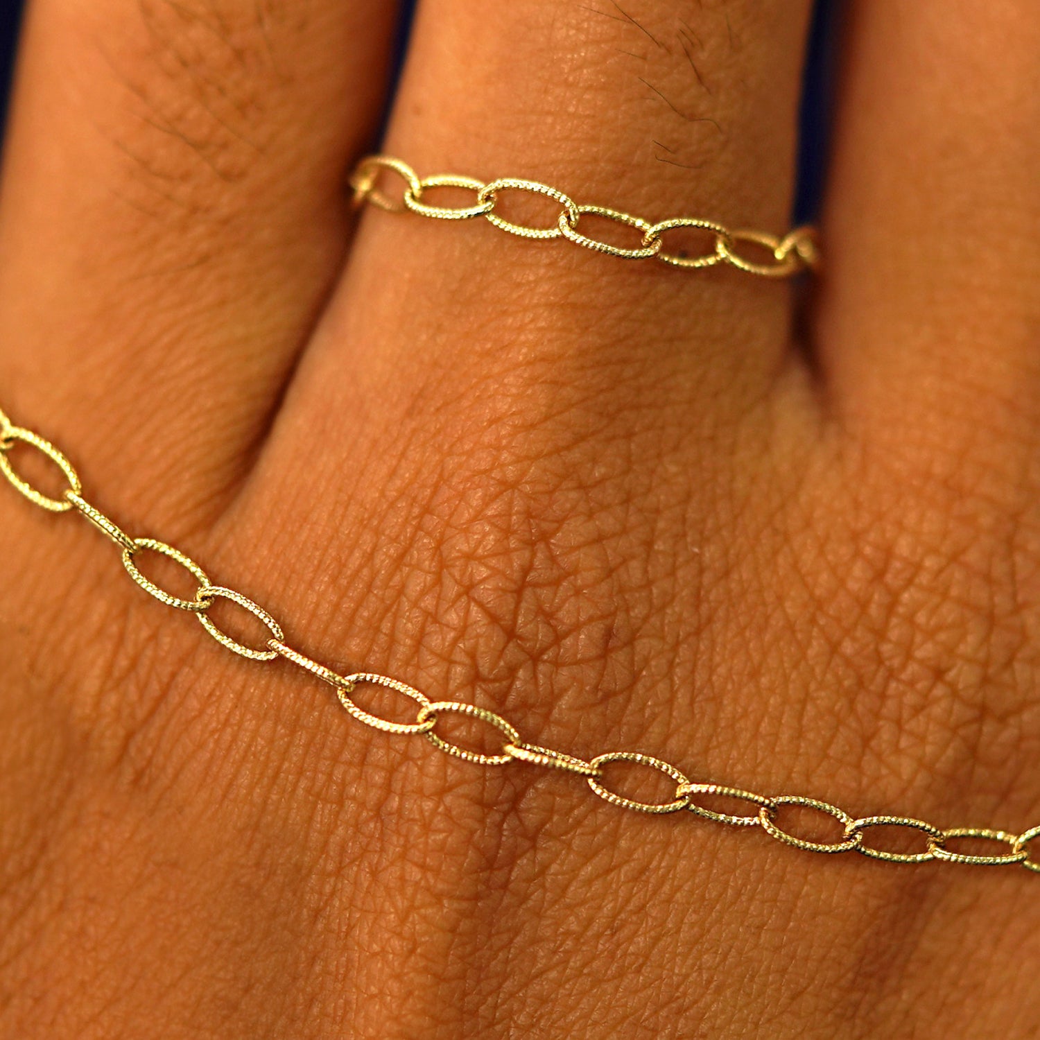 Close up view of a model's hand wearing a solid yellow gold Veren Ring and holding a Veren Bracelet