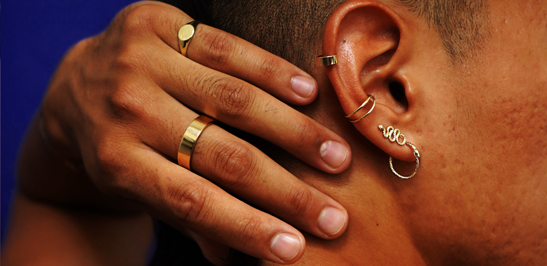A model with their hand on the back of their head wearing  Automic Gold rings, earrings, and ear cuff in 14k yellow gold