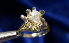 A 14k solid yellow gold ring with claw prongs in the shape of a hand gripping a raw diamond