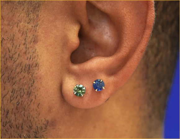 Close up view of a model's ear wearing an Emerald Earring and a Sapphire Earring in two lobe piercings