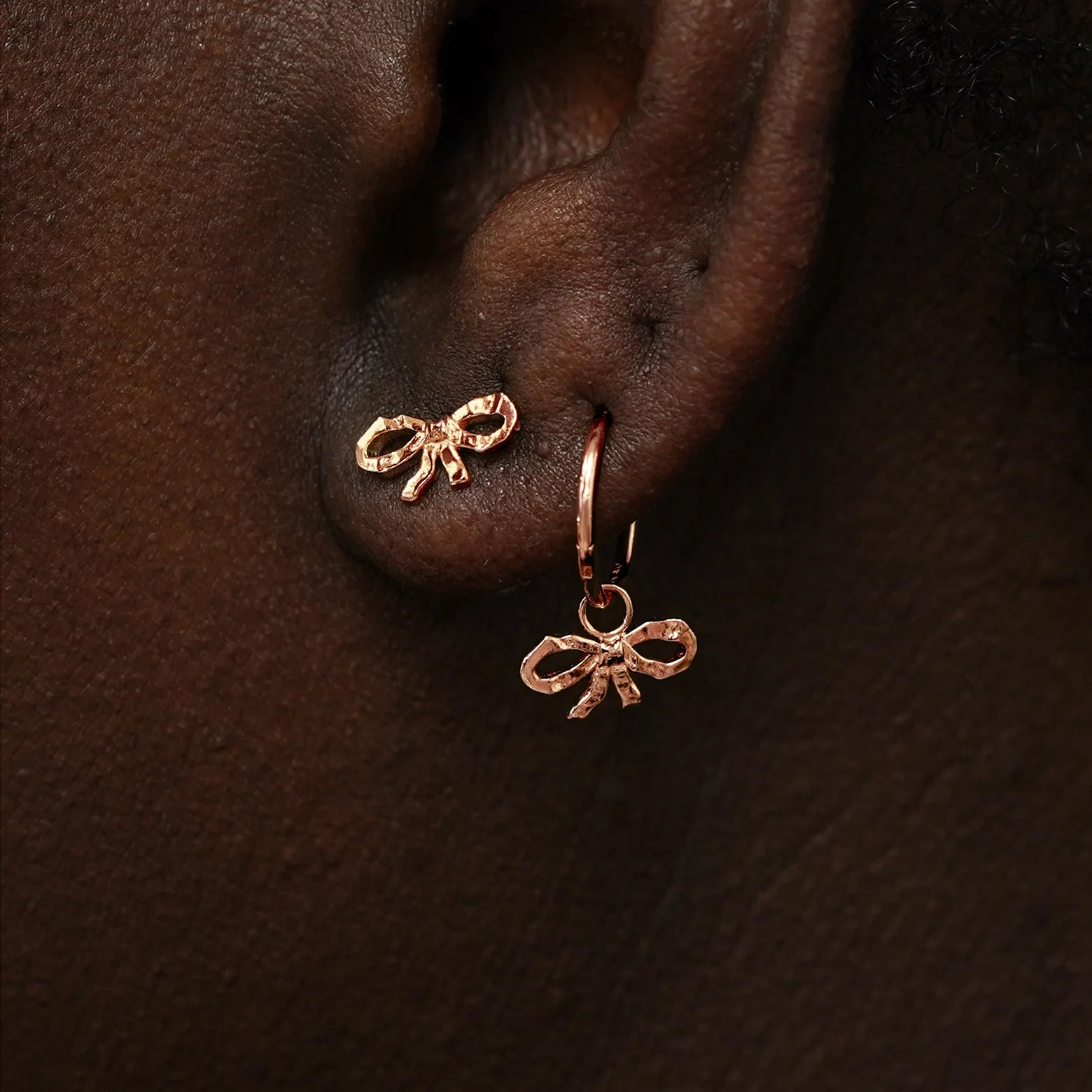 A model wearing a Bow Earring and a rose gold Bow Charm on a rope huggie hoop