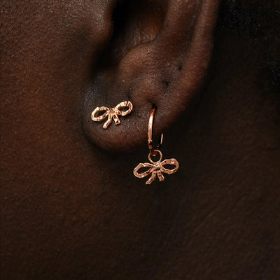 A model wearing a Bow Earring and a rose gold Bow Charm on a rope huggie hoop