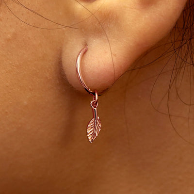 Close up view of a model's ear wearing a rose gold Leaf Charm on a Small Seamless Huggie Hoop