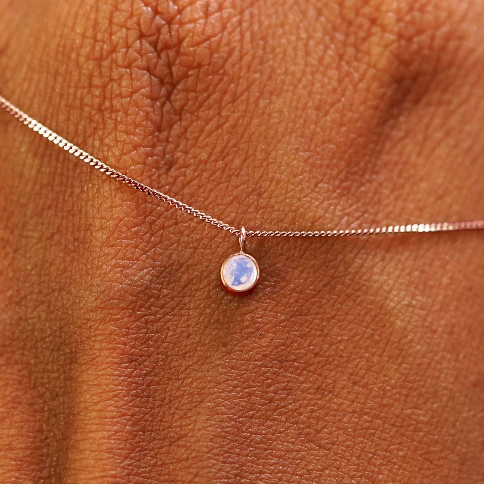 Close up view of a 14k rose gold Moonstone Necklace draped across the back of a model's hand
