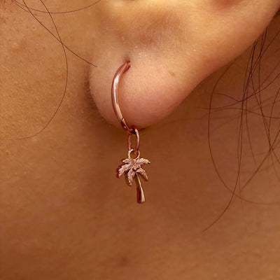 Close up view of a model's ear wearing a rose gold Palm Tree Charm on a Small Seamless Huggie Hoop