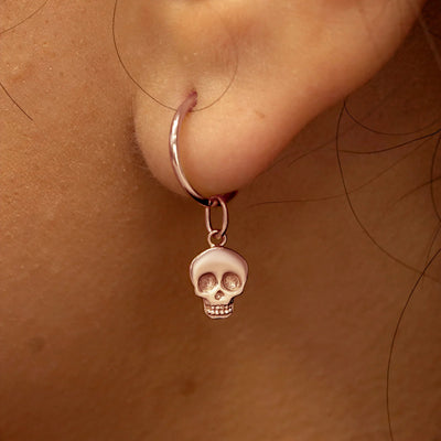 Close up view of a model's ear wearing a rose gold Skull Charm on a Small Seamless Huggie Hoop