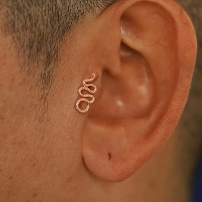 Close up view of a model's ear wearing a rose gold Snake Flatback in a tragus piercing