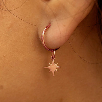 Close up view of a model's ear wearing a rose gold Starburst Charm on a Small Seamless Huggie Hoop