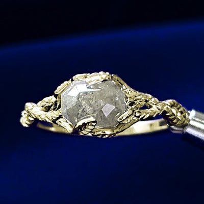 An octagon salt and pepper diamond held with leaf-shaped prongs on a band of twisted branches made from 14k champagne gold