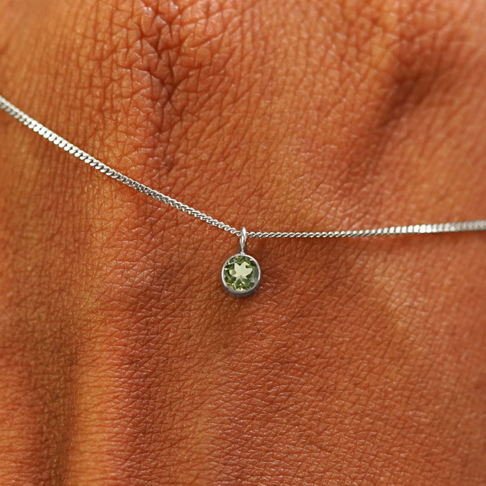Close up view of a 14k white gold Peridot Necklace draped across the back of a model's hand