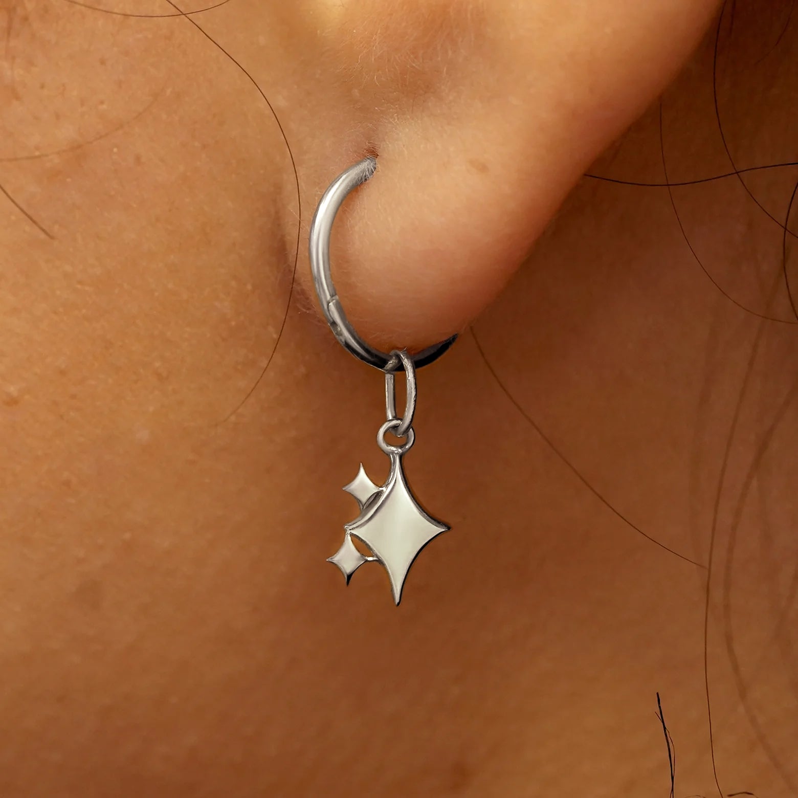 Close up view of a model's ear wearing a white gold Sparkly Emoji Charm on a Small Seamless Huggie Hoop