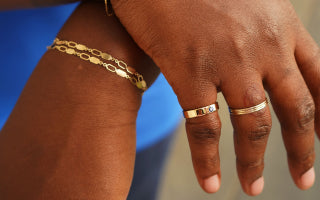 A model's hand crossed over their wrist Wearing a Gemstone Industrial Band, three stacked Line RIngs and two Tanlah Bracelets