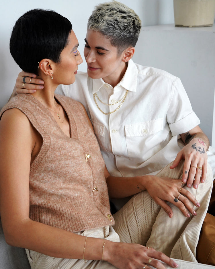 Two model's sitting and looking into each other's eyes while wearing various Automic gold 14k gold jewelry