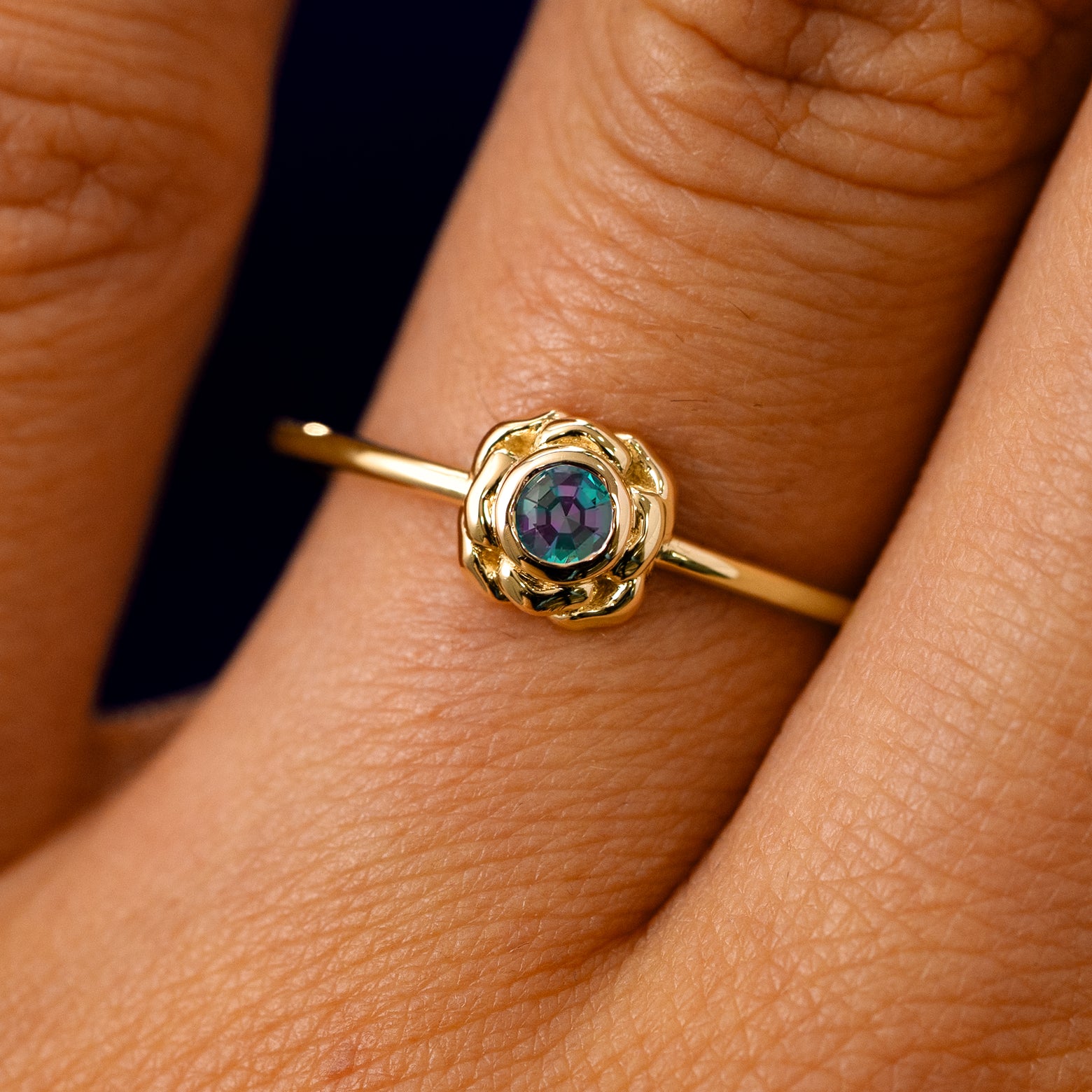 A solid 14k yellow gold Lab Alexandrite Gemstone Flower Ring on a model's finger