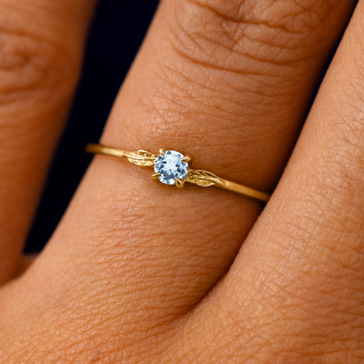 A solid 14k yellow gold Aquamarine Gemstone Two Leaf Ring on a model's finger
