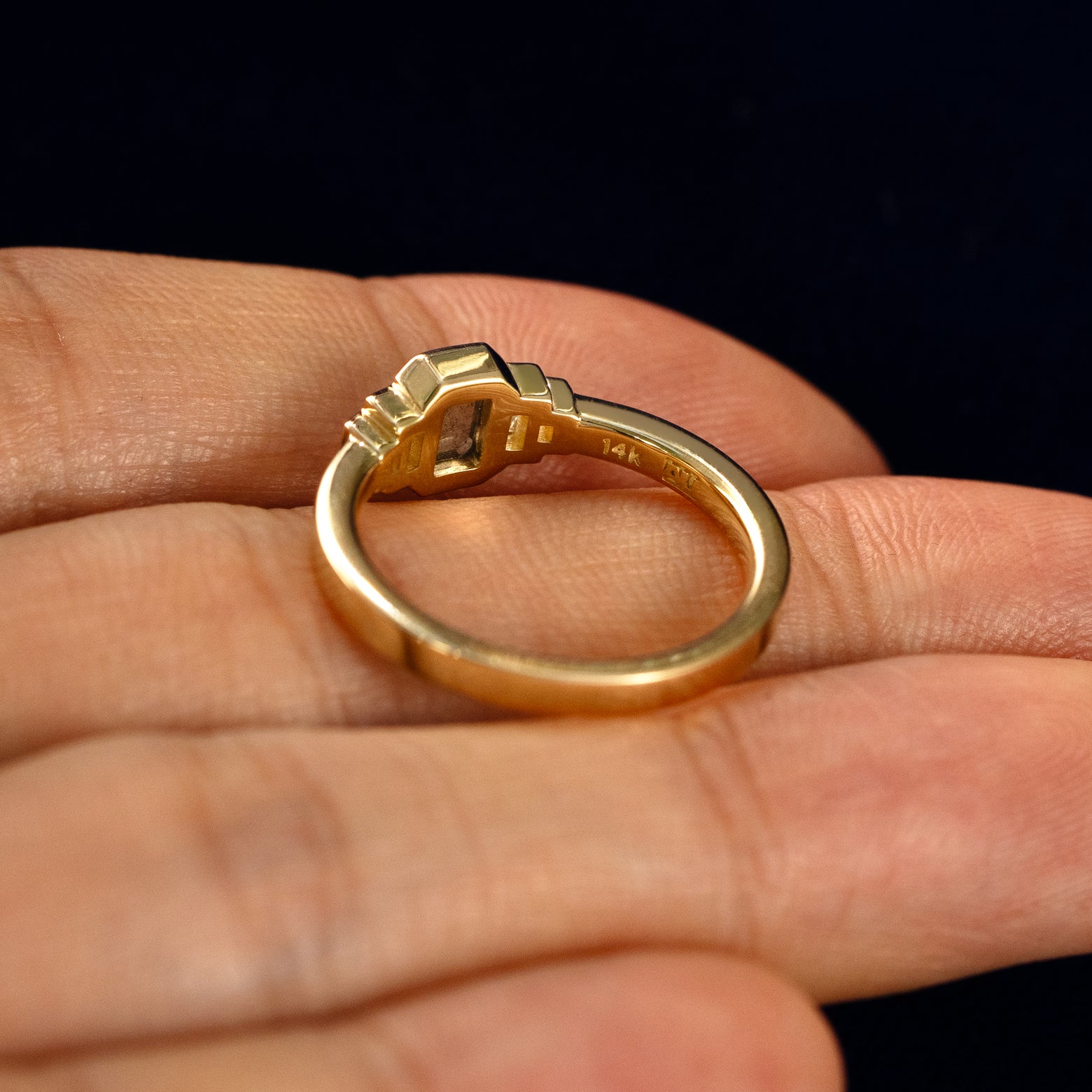 An Emerald Cut Salt and Pepper and Clear Baguette Diamond Ring in a model's hand showing the underside of the stones