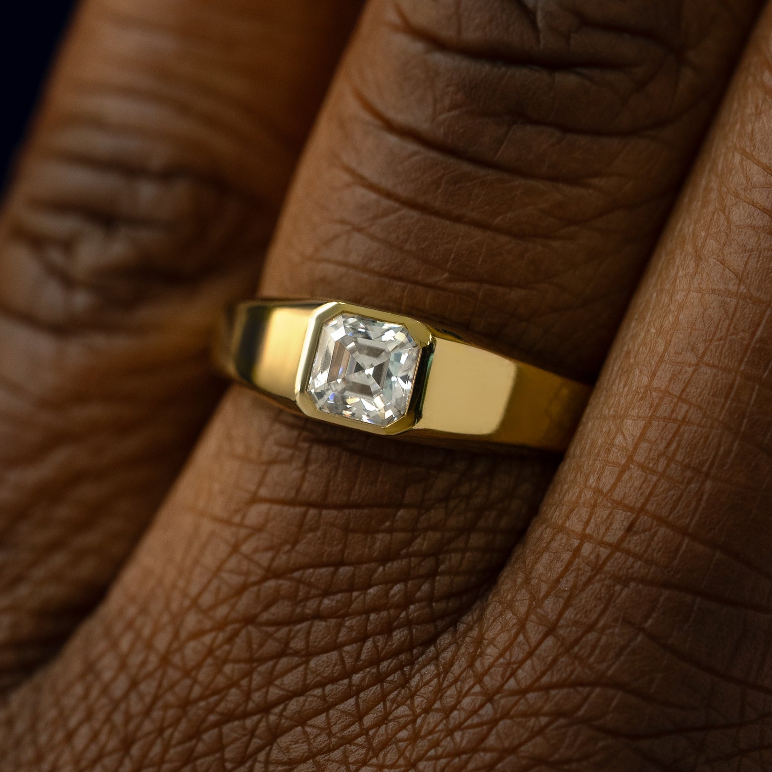 Close up view of a models hand wearing a solid gold asscher lab moissanite ring