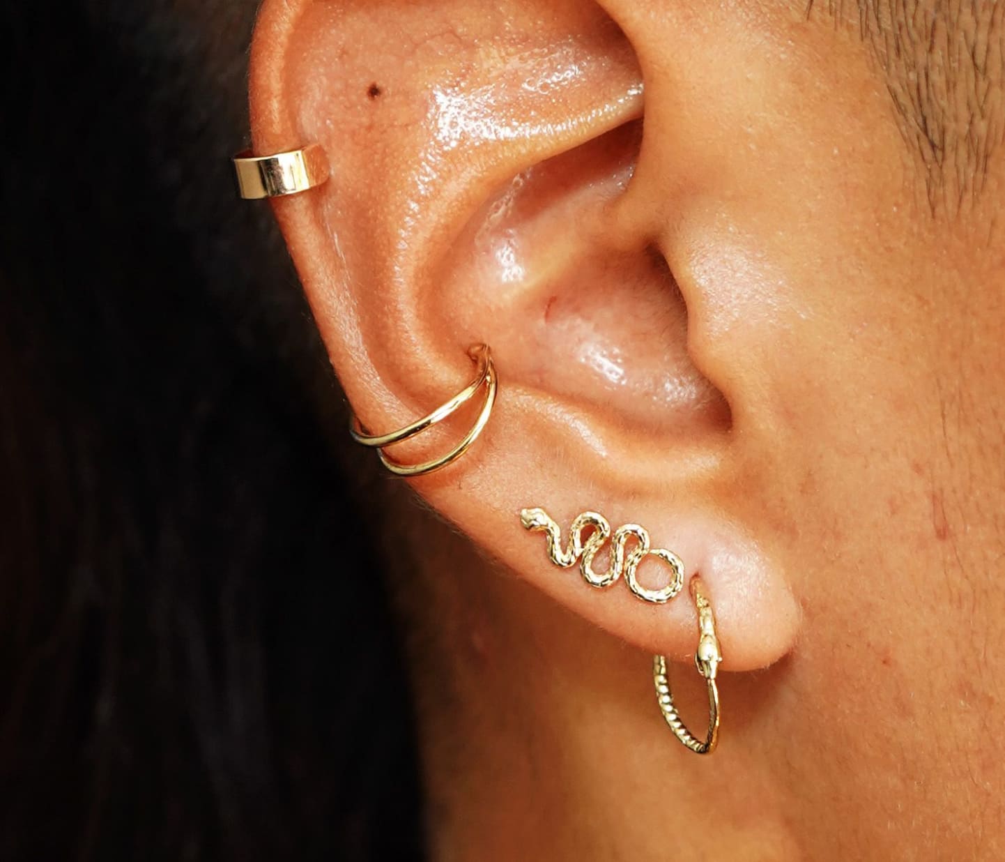 Close up view of a model's ear wearing a Snake Hoop, Snake Earring, and two yellow gold ear cuffs