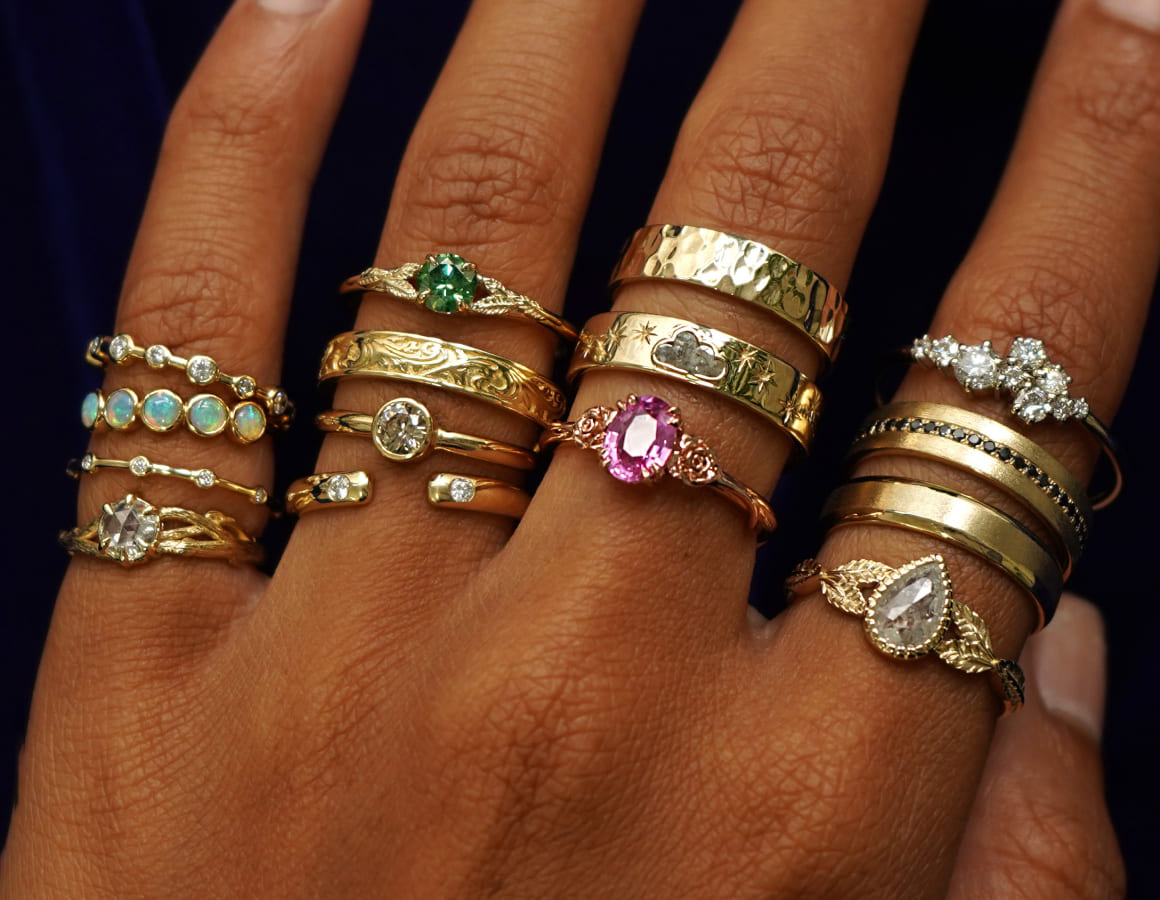 A model's hand wearing several different recycled solid gold engagement rings and wedding bands on each finger