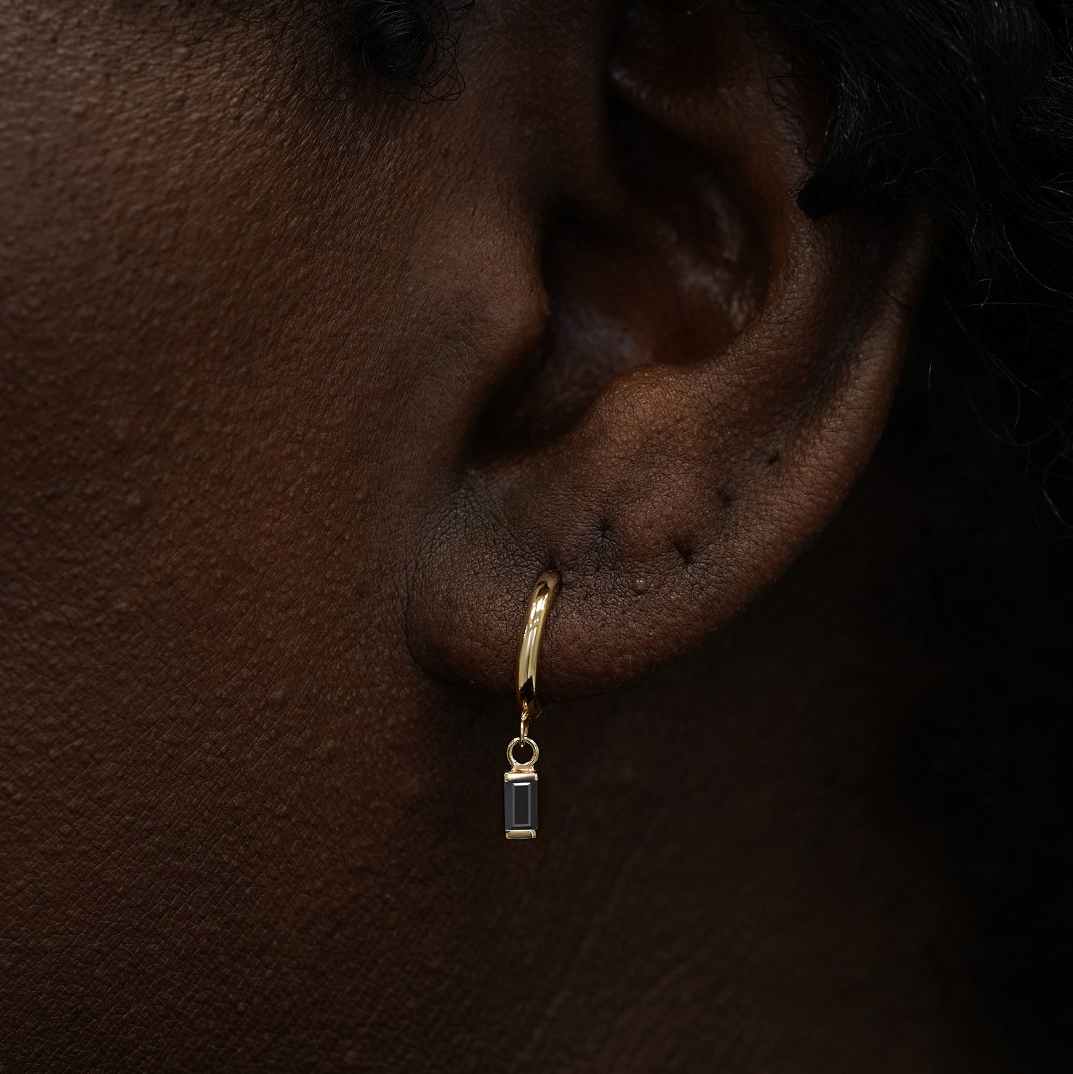 A model wearing a solid 14k gold baguette black diamond charm hoop earring