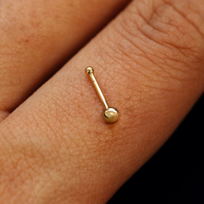 Close up view of a single 14k solid gold Ball Nose Stud with a ball end backing resting on the back on a model's hand