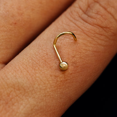 Close up view of a single 14k solid gold Ball Nose Stud with a twist corkscrew backing resting on the back on a model's hand