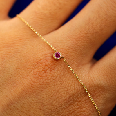 A pink sapphire bezel set gemstone necklace laying over a the back of a models hand to show the details of the chain