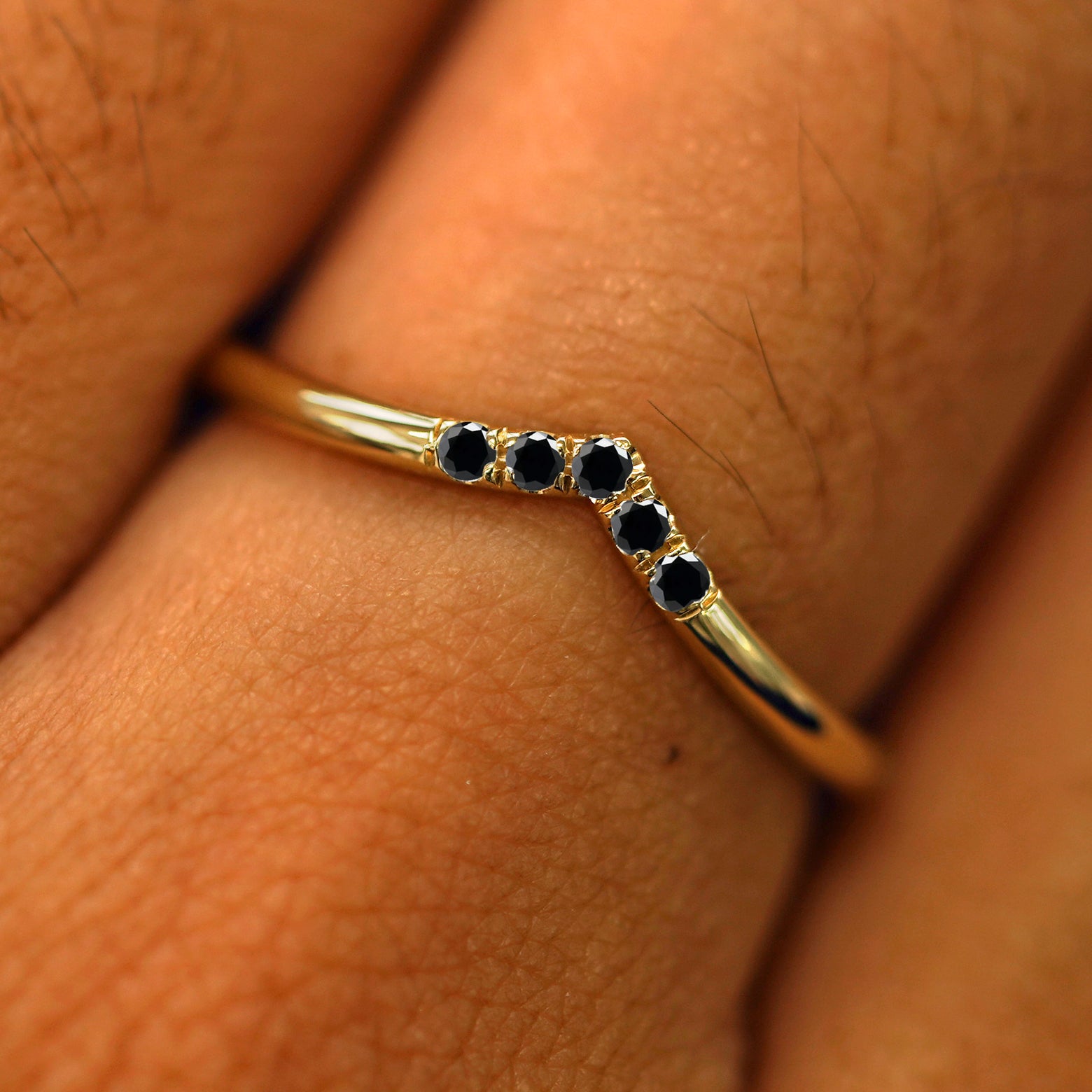 Close up view of a model's fingers wearing a 14k yellow gold Black Diamond Chevron Band