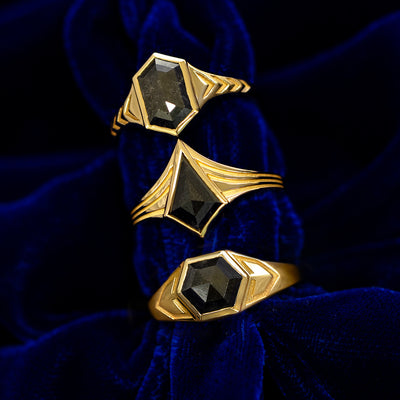 Three yellow gold black diamond engraved masculine rings stacked on a dark blue cloth