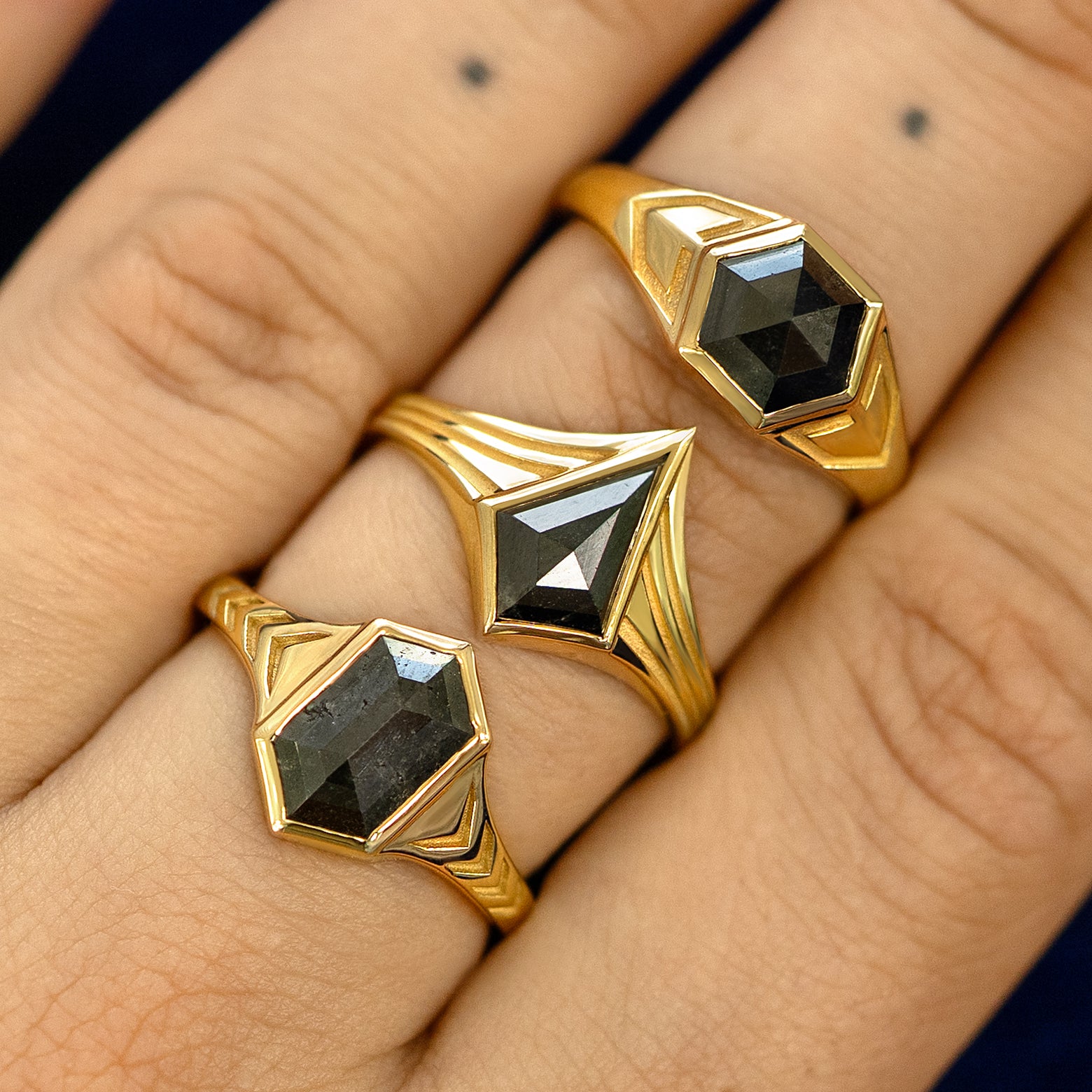 Close up view of a model's hand wearing three engraved solid gold black diamond masc engagement rings stacked on one finger
