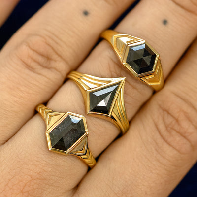Close up view of a model's hand wearing three engraved solid gold black diamond masc engagement rings stacked on one finger