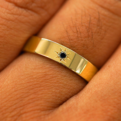 Close up view of a model's hand wearing a solid yellow gold Engraved Star Black Diamond Band