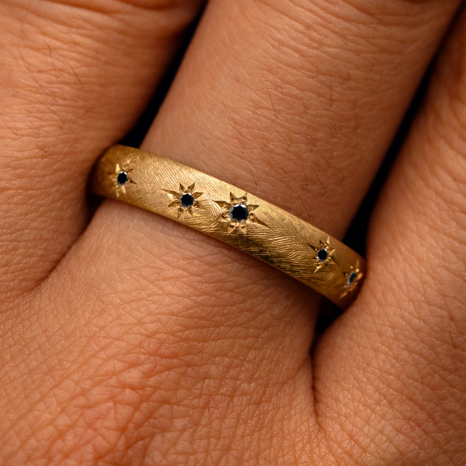 Close up view of a model's fingers wearing a 14k yellow gold Curvy Black Diamond Stars Velvet Band