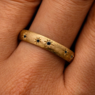 Close up view of a model's fingers wearing a 14k yellow gold Curvy Black Diamond Stars Velvet Band