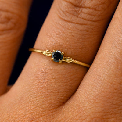 A solid 14k yellow gold Black Diamond Two Leaf Ring on a model's finger