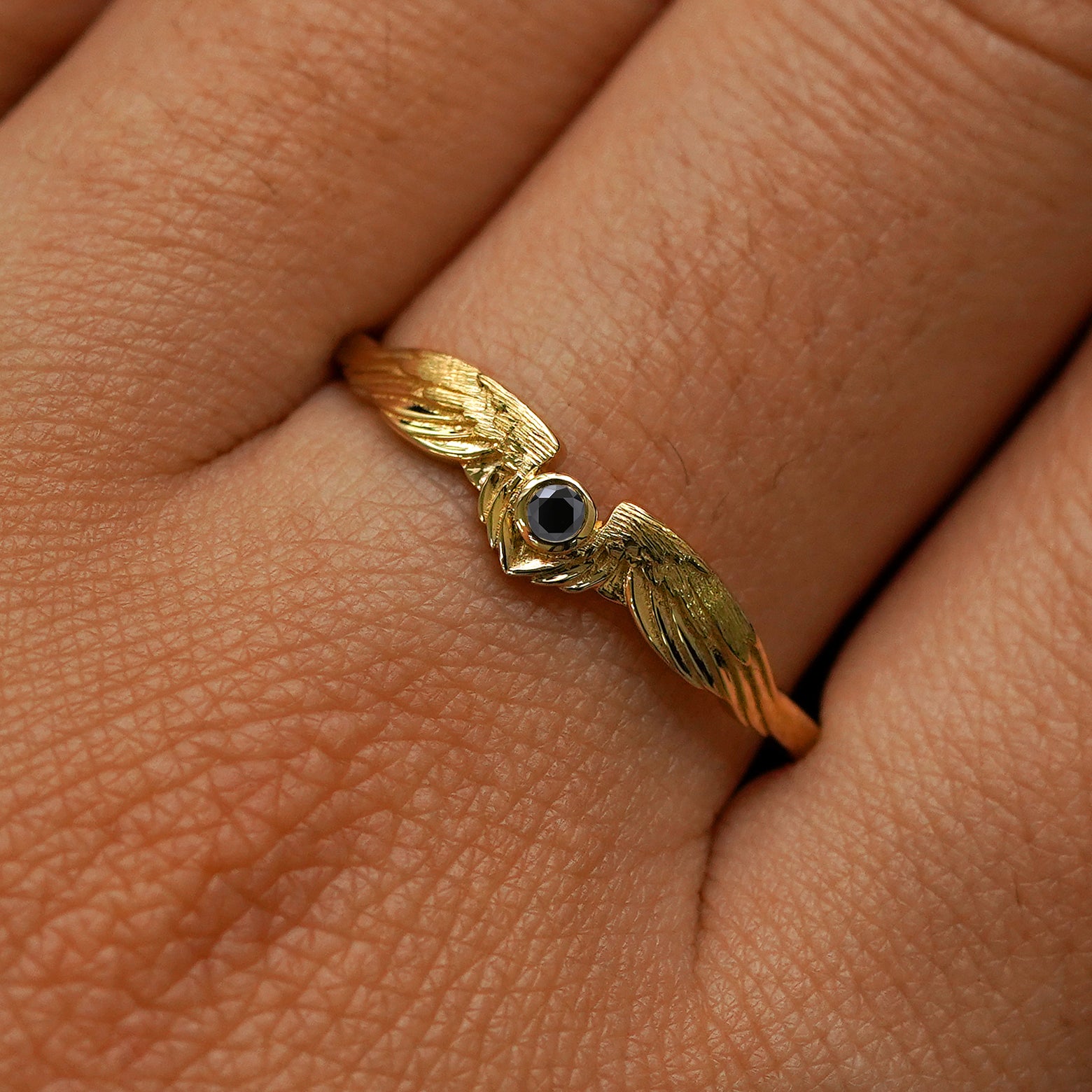 Close up view of a model's fingers wearing a 14k yellow gold Black Diamond Wings Ring