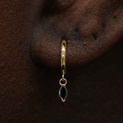 Close up view of a model's ear wearing a yellow gold Marquise Black Diamond Dangle Huggie Hoop