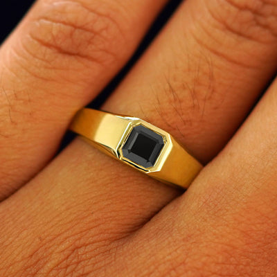 Close up view of a model's fingers wearing a yellow gold lab black moissanite Asscher Gemstone Signet Ring