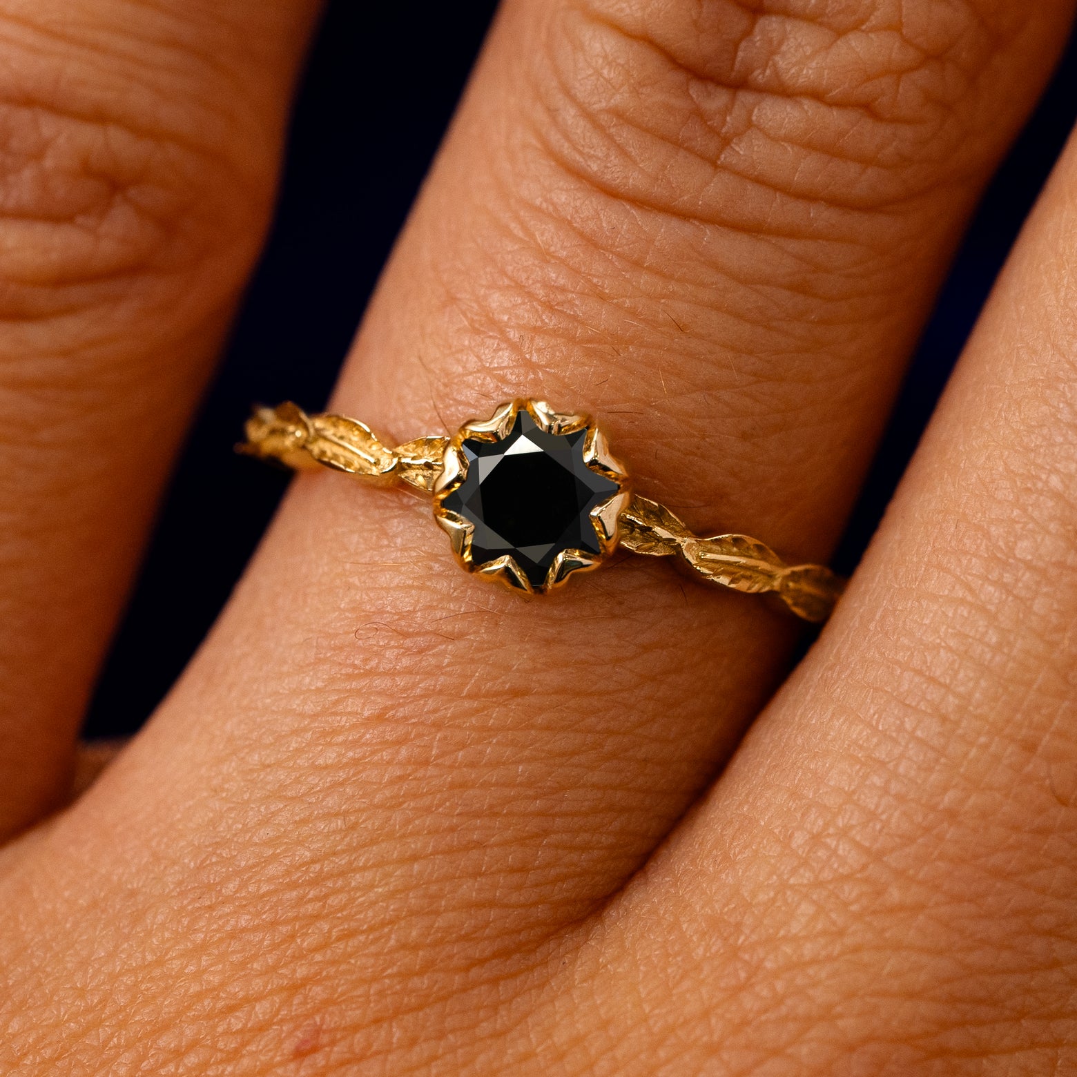 A solid 14k yellow gold Black Moissanite Leaf Ring on a model's finger