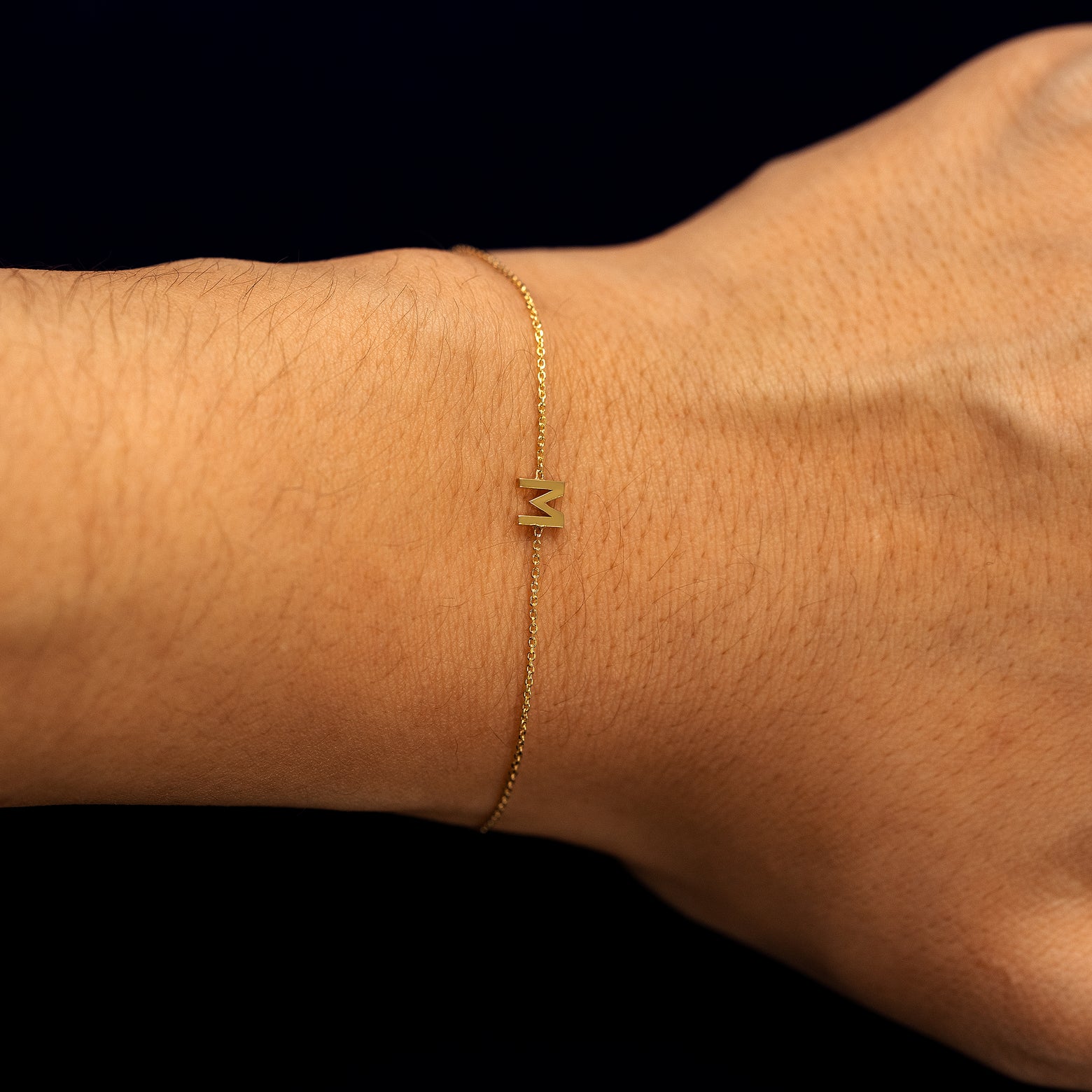 A models wrist wearing a solid gold block initial letter M bracelet
