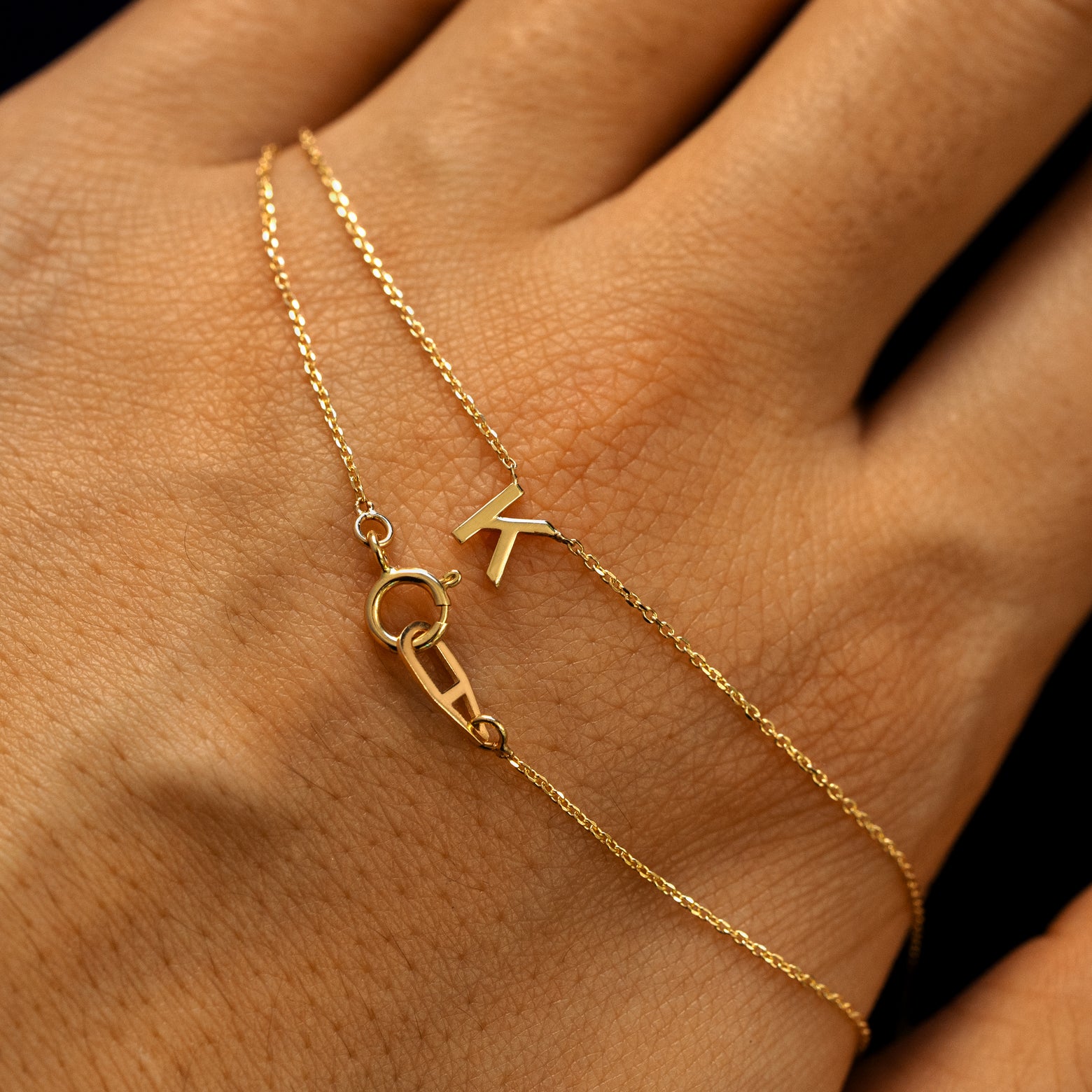 A letter K block initial cable chain necklace wrapped twice around a models hand