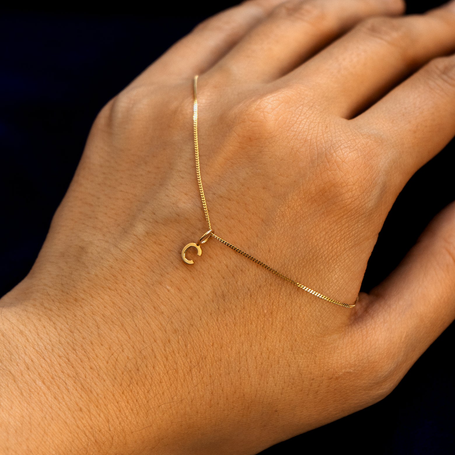 Close up view of a model's hand with a 14k gold letter C Initial Charm on a Mini Miami Chain