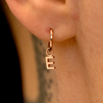 Close up view of a model's ear wearing a 14k rose gold Seamless Huggie Hoop with a letter E block initial charm