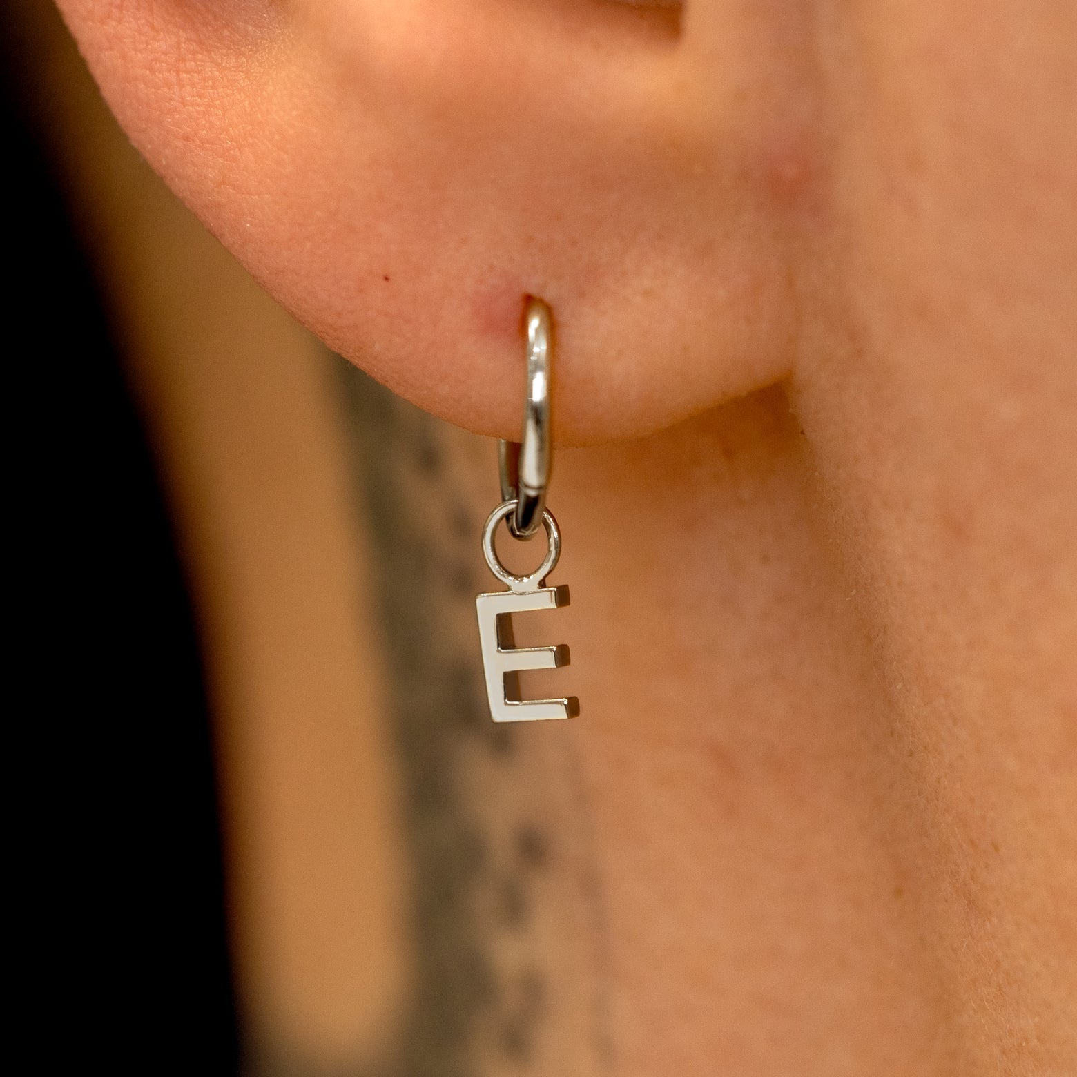 Close up view of a model's ear wearing a 14k white gold Seamless Huggie Hoop with a letter E block initial charm