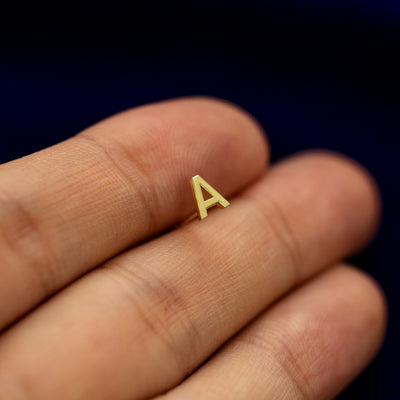 A solid yellow gold Block Initial Earring  in the letter A held in between model's fingertip to show the detail of the intial