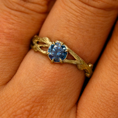 Close up view of a model's fingers wearing a 14k yellow gold Blue Moissanite Branches Ring