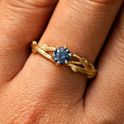 Close up view of a model's fingers wearing a 14k yellow gold Blue Moissanite Branches Ring