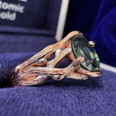 A photo of 14k Rose Gold Branch-prongs-set ~7x5.5mm Oval Dark Green Sapphire on Tapered Tree-inspired Band Custom Ring in a blue ring box