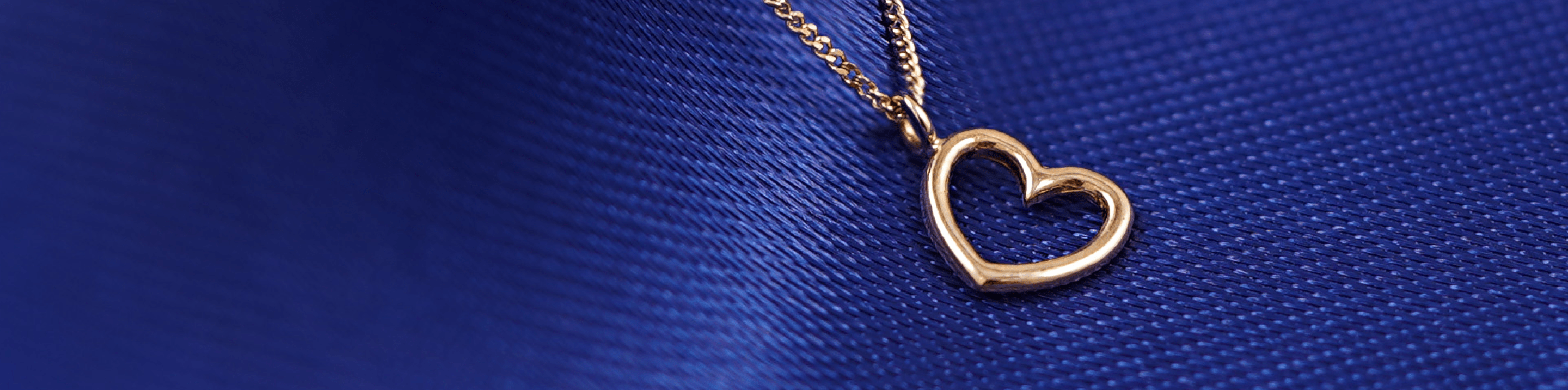 A solid 14k yellow gold Open Heart Charm on an Essential chain resting on a blue cloth background