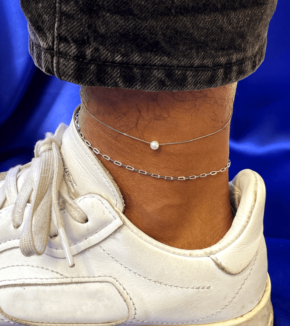 Close up view of a model's ankle wearing a Pearl Slide Anklet and a Butch Anklet both in 14k white gold